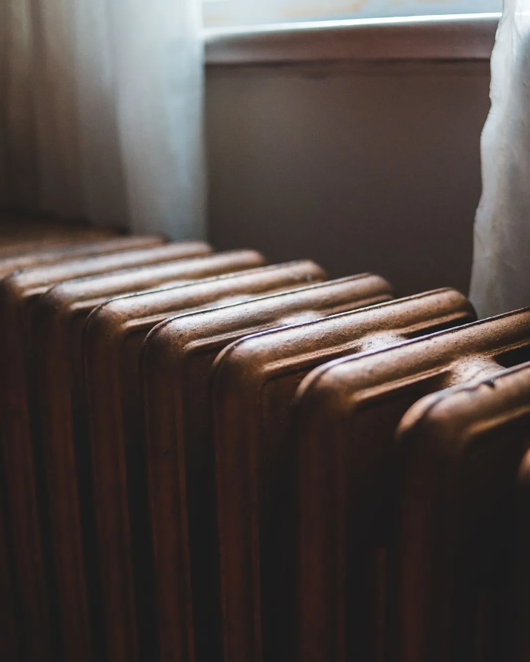 Vieux radiateur en fonte sous une fenêtre ancienne voilée d'un rideau
