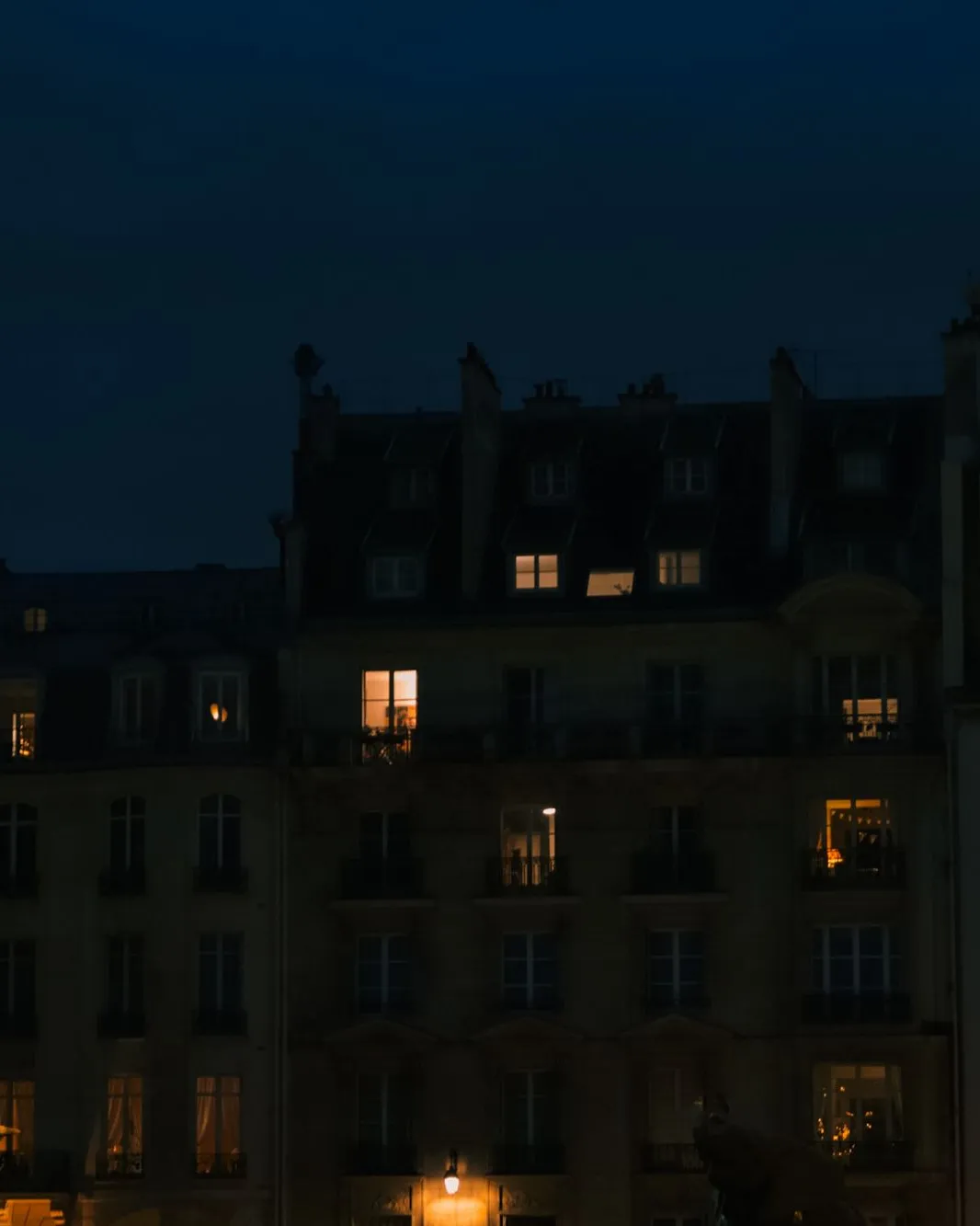 Immeuble parisien ancien à la tombée de la nuit, plusieurs fenêtres éclairées