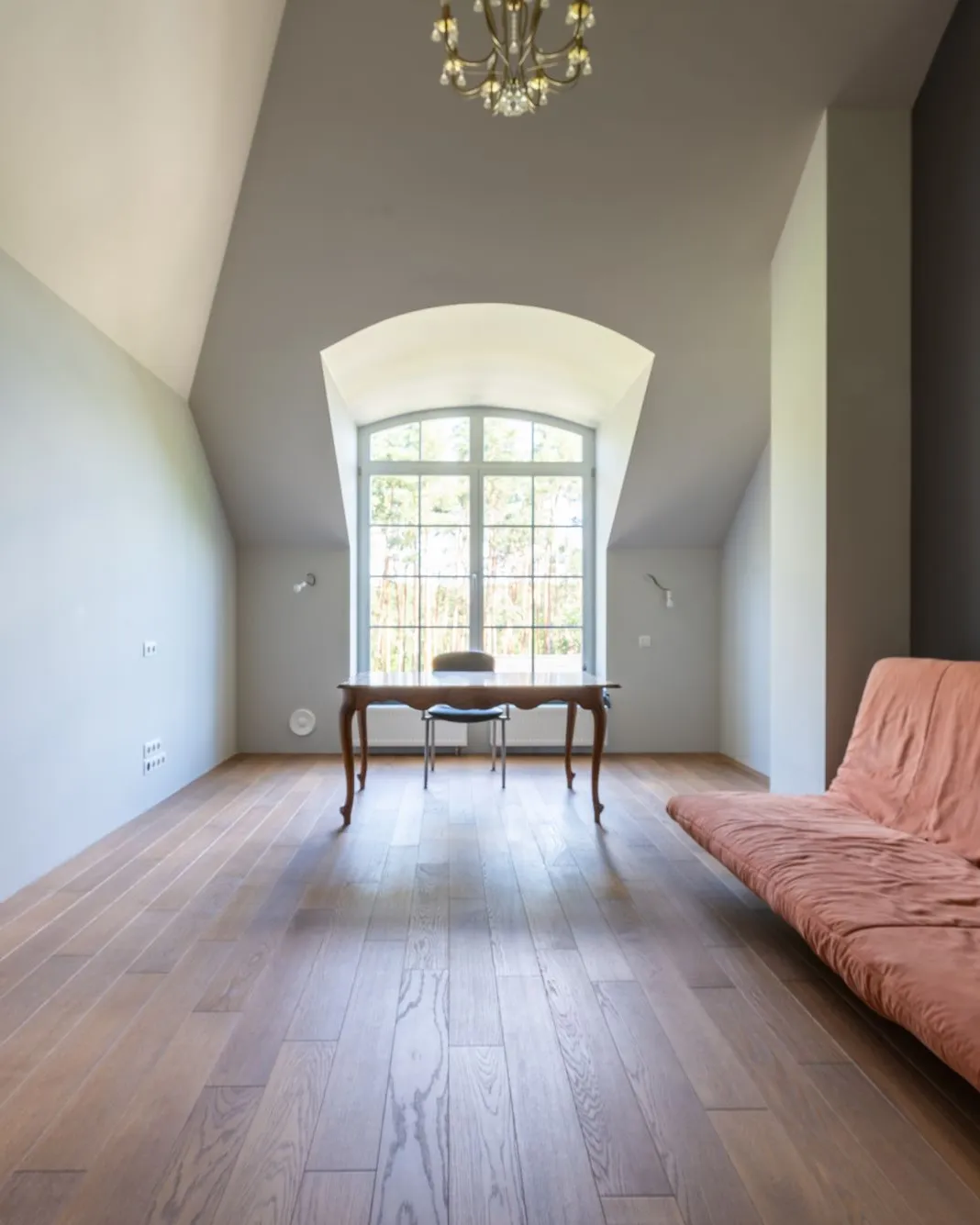 Pièce inoccupée au parquet ancien, éclairée par une fenêtre cintrée, presque vide de meubles